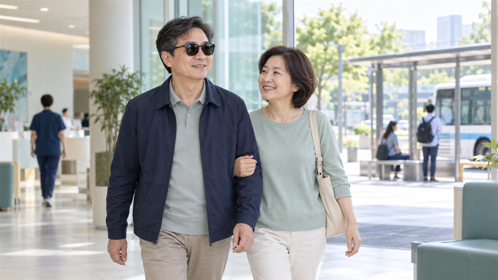 선글라스를 쓴 사람이 밝은 병원 로비에서 동행인과 함께 걸어 나가고 있다